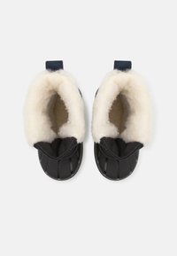 Botines impermeables negros con suave forro de felpa beige y suela texturizada. Cuenta con un puño doblado y una pestaña para ponerlos fácilmente.