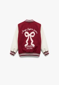 Bordeaux og hvid varsity jakke med en stor hvid sløjfe og tekst, der siger "Altid Glad i London" og "London Est. 1982," med stribede mansjetter.