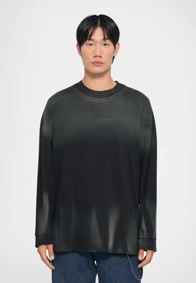 Camiseta negra de manga larga con cuello redondo, que presenta una textura degradada y un logo bordado en azul en el pecho.