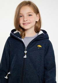 Marinblå zip-up jacka med fleece-fodrad huva, prydd med en gul paraplylogotyp och dekorativa dragband med tofsar.