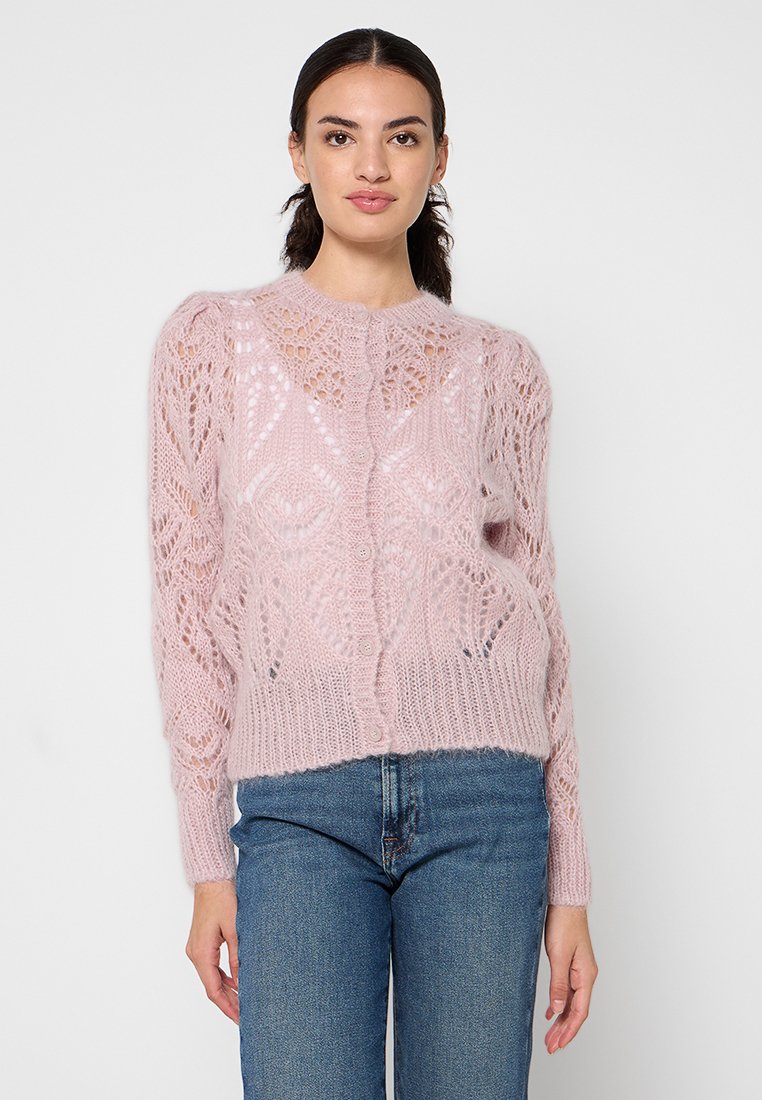 Jasnoróżowy sweter dzianinowy z misternymi koronkowymi wzorami, okrągłym dekoltem i zapięciem na guziki. Noszony na niebieskich dżinsach.