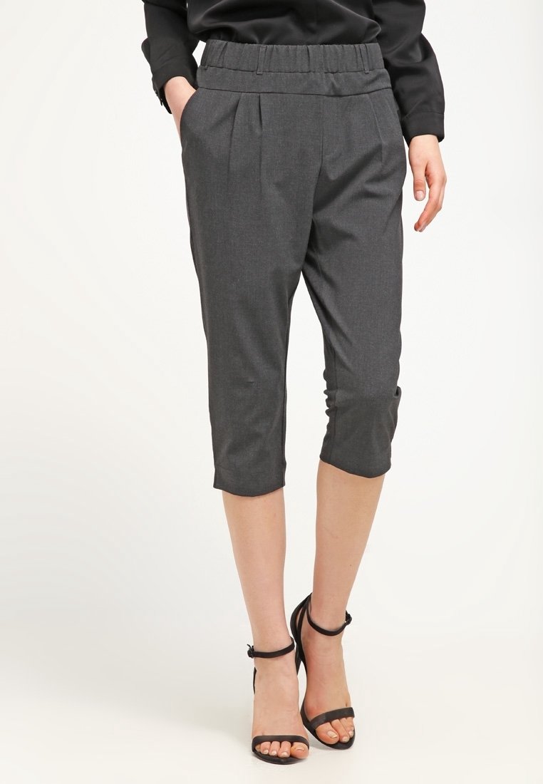 Harmaat lyhyet housut, joissa on poimutettu etuosa, joustava vyötärö ja nilkkapituiset lahkeet. Suora kangas, yhdistettynä mustiin remmikorkokenkiin.