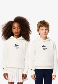 Felpe con cappuccio a girocollo in panna chiara, con logo Lacoste nero, polsini a coste e piccolo ricamo di coccodrillo verde sulle maniche.
