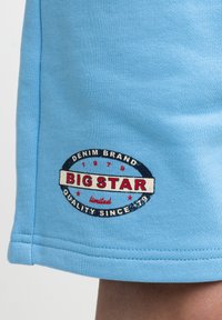Světle modré látkové šortky mají kruhové vyšívané logo s texty "BIG STAR", "DENIM BRAND" a "QUALITY SINCE 1979" v kontrastních barvách.