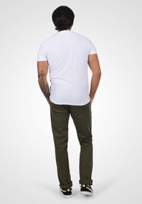 Hvit t-skjorte med korte ermer, olivengrønne rutete bukser og svarte joggesko med beige detaljer. Viser en ren, uformell stil fra baksiden.