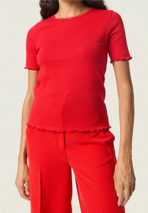 Haut rouge à manches courtes avec encolure ronde, tissu texturé et poignets à volants. Associé à un pantalon large rouge assorti.