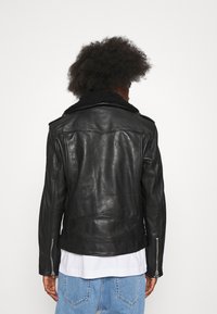 Sort læder bikerjakke med en shearling-krave, lynlåse ved håndleddene og en glat tekstur. Jakken har et tætsiddende design og minimal syning.