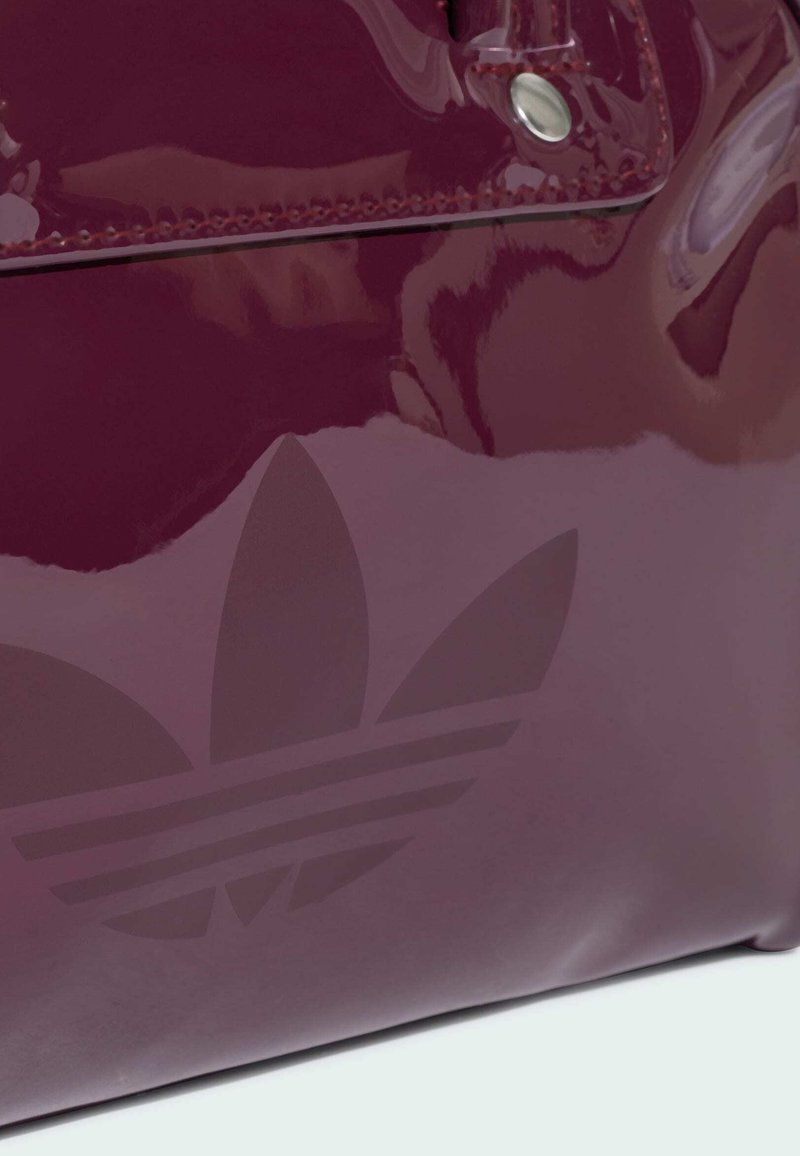 Borsa Adidas bordeaux lucida con patta cucita, bottone a scatto metallico e logo trefoil in rilievo sulla superficie.