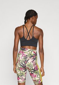 Sujetador deportivo negro con tirantes cruzados en la espalda, combinado con mallas de cintura alta con un estampado floral en tonos verdes y rosas.