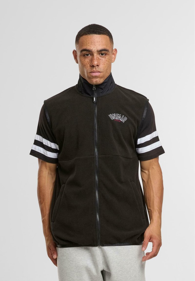 Gilet en polaire noir avec un col haut, une fermeture éclair à l'avant et des poches latérales ; présente des accents rayés blancs sur les manches courtes et un logo brodé.