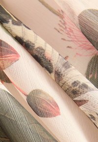 Nærbillede af transparent stof med et blomsteret mønster med blade og knopper i dæmpede grønne, pink og beige nuancer.