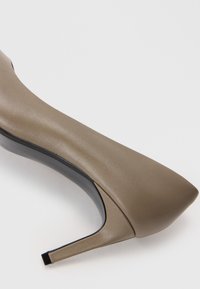 Μυτερή γόβα σε ταμπά δέρμα, με λεία υφή, λεπτό μαύρο τακούνι και διακριτές σχεδόν λεπτομέρειες σχεδίασης.