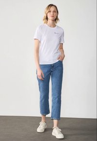 White short-sleeve t-shirt with "love" printed in black, paired with blue cropped jeans and white sneakers on a gray floor.