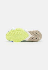 Semelle extérieure de chaussure de sport présentant une combinaison de surfaces en caoutchouc jaune, verte et neutre avec des motifs texturés pour l'adhérence et la traction.