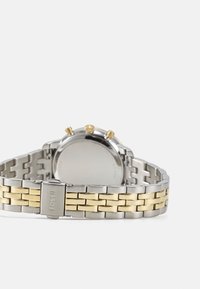 Silberne und goldene Metalluhr mit einem rechteckigen Armband, das abwechselnde Glieder aufweist, drei goldene Drücker und ein glattes, rundes Gehäuse.