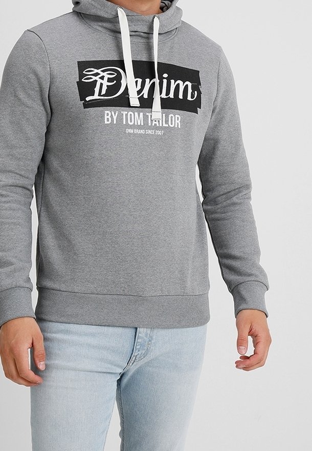 Homme portant un sweat à capuche gris clair avec des cordons blancs et un texte en noir et blanc "Denim by Tom Tailor", associé à un jean bleu clair.