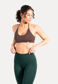 Sujetador deportivo marrón con tirantes finos, con una textura suave. Combinado con leggings verdes de cintura alta que presentan un patrón sutil en el lateral.