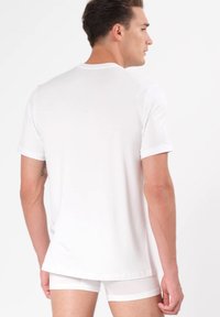 Hvid kortærmet t-shirt lavet af glat stof, med en rund halsudskæring og en standard pasform, præsenteret med matchende hvide undertøjsdele.