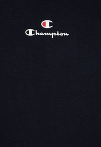 Μπλουζάκι από βαμβάκι σε ναυτικό μπλε χρώμα με λευκό λογότυπο "Champion" και κόκκινη λεπτομέρεια, διαθέτοντας απαλή υφή και κανονικό σχέδιο κοντού μανικιού.