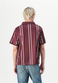 Kortermet polo skjorte i burgunder med vertikale hvite striper. Glatt tekstur, avslappet passform og klassisk krage design.