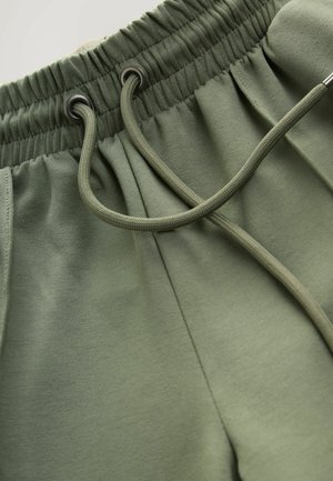 Tamsiai žali sportiniai šortai su elastingu juosmeniu, kuris turi raištį su metaliniais galiukais ir minkšta tekstūra.