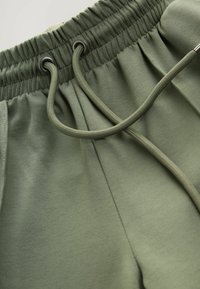 Olive rohelised dressipüksid elastse vöökoha ja metallsulguritega nööriga, millel on pehme tekstuur.