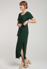Robe midi verte avec des manches courtes et un lien à la taille ; présente une fente haute, une texture de tissu douce et un col rond.
