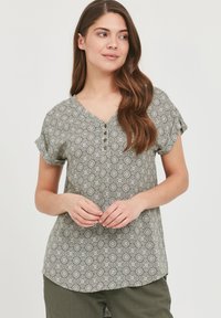 Kortærmet bluse i blødt stof med et grønt og hvidt cirkulært mønster, V-hals-design og tre-knaps placket fortil.