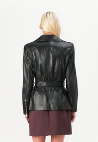 Black leather jacket with a tailored fit, featuring a belted waist, zippered pockets, and a standard collar. Smooth texture and structured design.