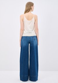 Light cream tank top with spaghetti straps paired with high-waisted, wide-leg blue denim jeans featuring a raw hem and back pockets.
