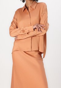 Camisa de tela suave color melocotón con cuello y botones en la parte delantera. Combinada con una falda a juego, ambas con un corte relajado.