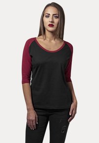 Svart t-skjorte med trekvart ermer og burgunder raglan-ermer. Mykt stoff med rund hals og en avslappet passform. Slitte jeans.