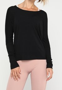 Schwarzes Langarmshirt mit weitem Ausschnitt und engen Bündchen, aus weichem Stoff gefertigt. Übereinander getragen mit hellrosa Leggings.