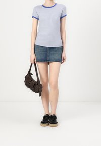 Chemise à rayures bleues et blanches à manches courtes avec bord bleu, mini-jupe en denim, baskets noires et sac en cuir brun avec des accents texturés.