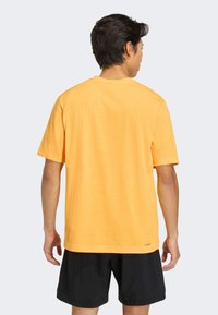 Kurzärmeliges T-Shirt mit Rundhalsausschnitt aus leuchtend orangefarbenem Baumwollstoff. Verfügt über eine lockere Passform mit glatter Textur und einem kleinen Logo am Saum.