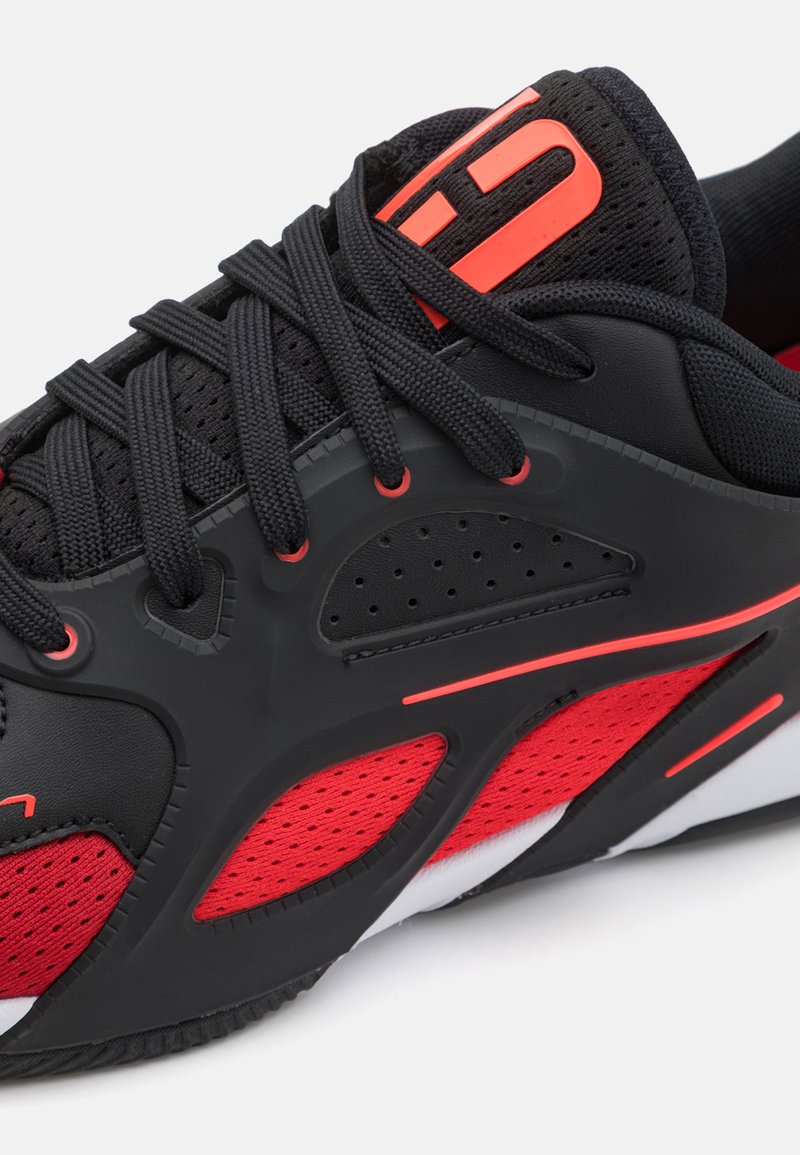 Schwarzer Sportschuh mit roten Akzenten, ausgestattet mit einem strukturierten Synthetik-Obermaterial, Mesh-Einsätzen und flachen Schnürsenkeln. Leichtes Design, das sich für den Sport eignet.
