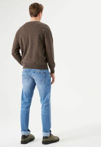 Pull en maille marron, jeans bleu clair avec les poignets retroussés, et baskets vertes. Vu de dos, mettant en valeur l'ajustement et le design de la tenue.