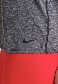 Szary sportowy T-shirt z czarnymi szwami i logo Nike, zestawiony z czerwonymi legginsami ozdobionymi fakturą w diamentowy wzór.