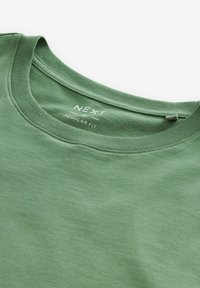 Camiseta de algodón verde con cuello redondo, corte regular. El texto impreso dentro del cuello dice "NEXT REGULAR FIT." Tejido suave y texturizado.