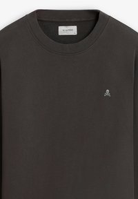 Chemise à manches longues gris foncé avec un col ras du cou, des poignets côtelés et un petit emblème blanc de skull et os croisés sur la poitrine.