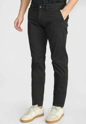 Chinos noirs ajustés en mélange de coton, avec une taille à boutons et deux poches avant, associés à des baskets blanches.