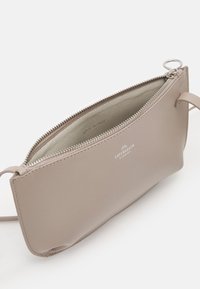 Bolso de mano beige con cremallera, hecho de cuero liso, con cremallera plateada y detalle de logo; el interior cuenta con un forro suave y un diseño minimalista.