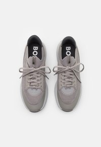 Grå atletiska sneakers med meshtyg på ovansidan, rundad tå och texturerad gummisula. Har tonala snören och varumärkesmärke på tungan.