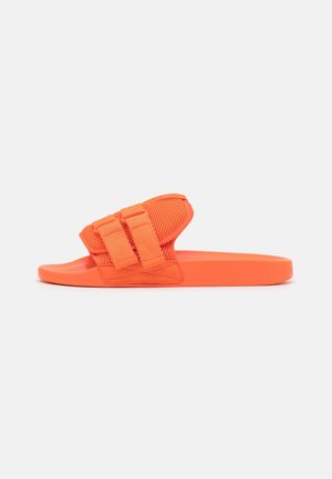 Pomarańczowa klapka na płaskiej podeszwie z teksturowaną podstawą, tkanym cholewką oraz dwoma regulowanymi paskami zapewniającymi pewne dopasowanie. Wykonana z materiałów syntetycznych.