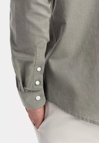 Camicia a maniche lunghe in tessuto verde tenue, con polsini abbottonati con bottoni bianchi e una finitura liscia e testurizzata. Vista laterale della manica.