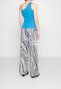 Niebieski top na ramiączkach z asymetrycznym projektem na jedno ramię, w połączeniu z szerokimi spodniami w czarno-białe paski zebry, gładki materiał, wysoki stan.