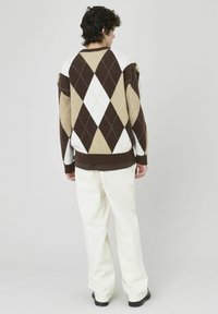 Pull en motif argyle marron, crème et beige avec des poignets et un ourlet côtelés, associé à un pantalon blanc ample.
