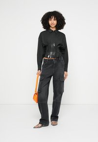 Mustad lühike särk läikiva viimistluse ja struktureeritud disainiga, kombineeritud tumedate cargo-pükstega, esile tõstetud õmblustega ning oranži käekotiga.