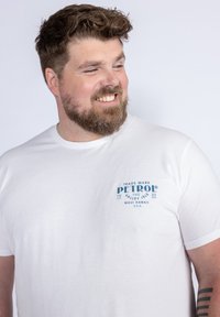 Bílý bavlněný tričko s modrým potiskem loga na levé hrudi. Kulatý výstřih a krátké rukávy, hladká textura.