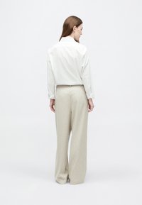 Cămașă albă cu guler și mâneci lungi, combinată cu pantaloni largi de culoare bej deschis, evidențiind texturi fine și croială ajustată.